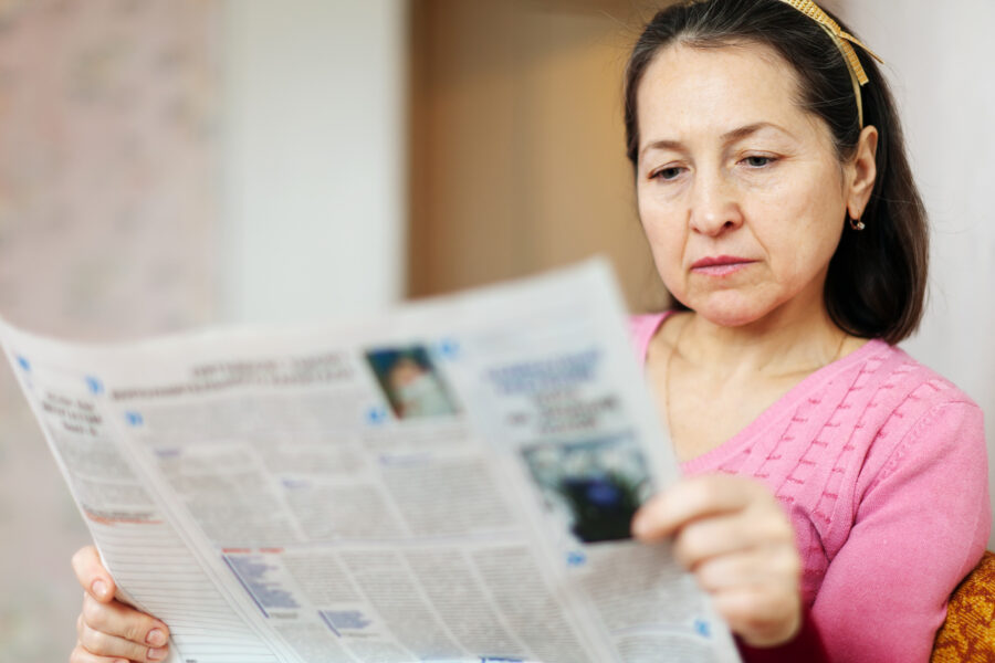 A woman reads a newspaper.