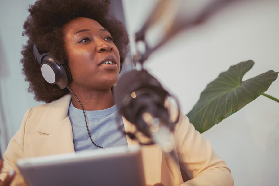 A Black woman with recording equipment speaks into a microphone