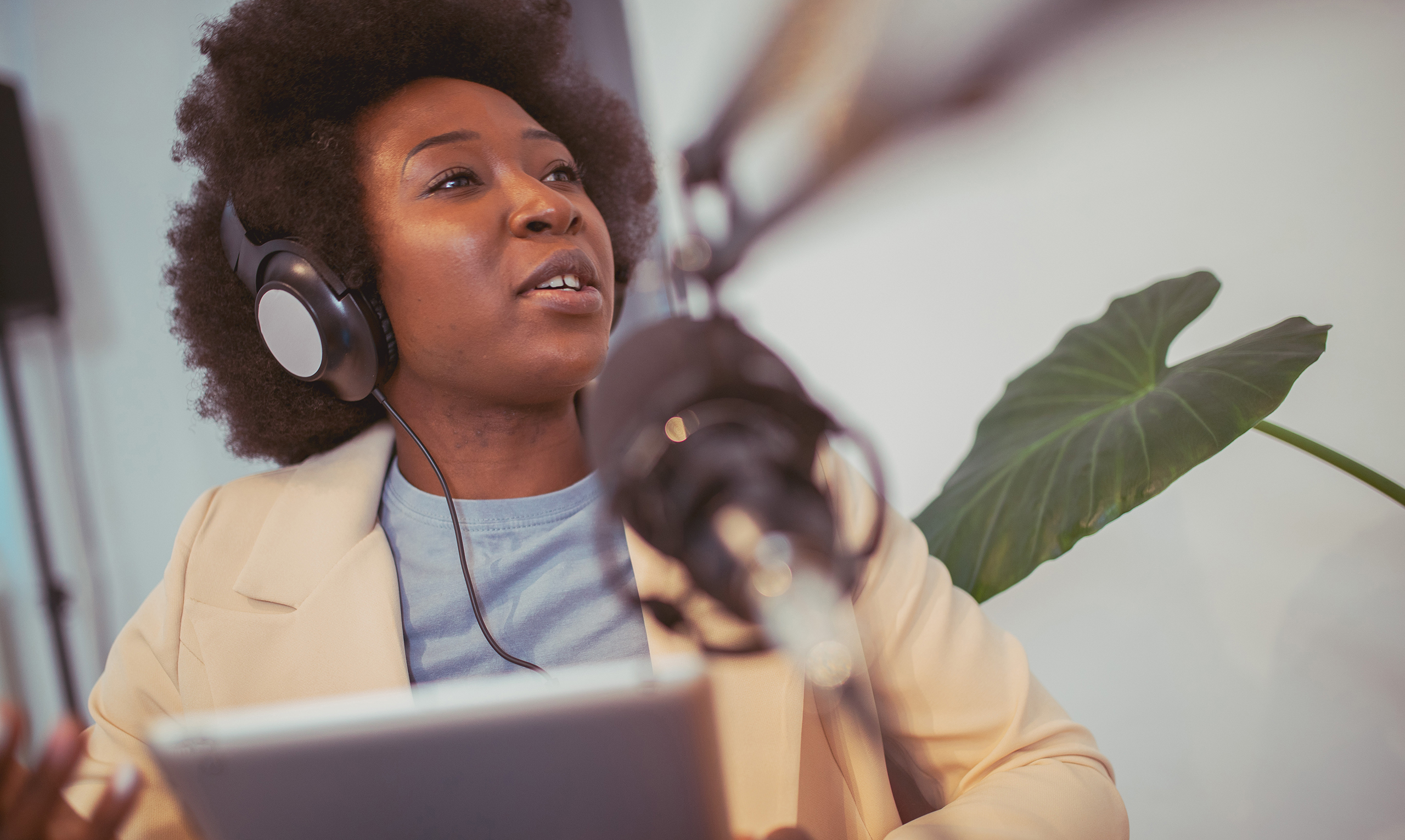 A Black woman with recording equipment speaks into a microphone